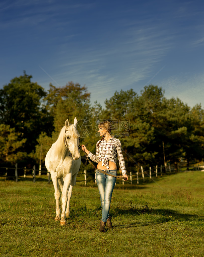 在牧场上骑着白马行走的年轻女子图片