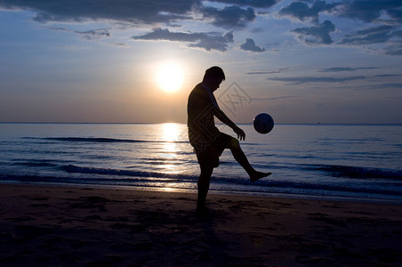 剪影男子在沙滩上踢足球图片