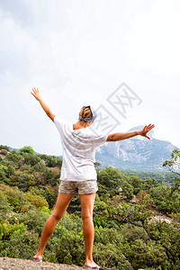 年轻快乐的女士站在岩石上举起手仰望图片