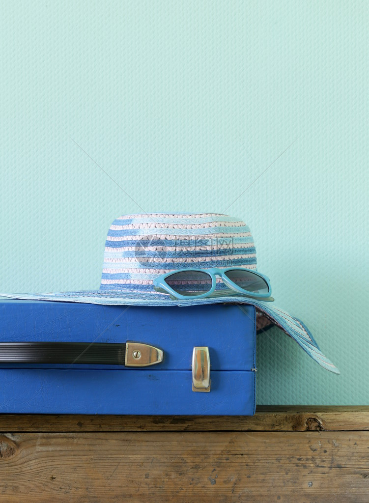 古老的蓝色行李箱旅行和海滩帽在绿图片