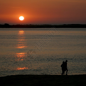 日落时在沙滩上散步的情侣图片