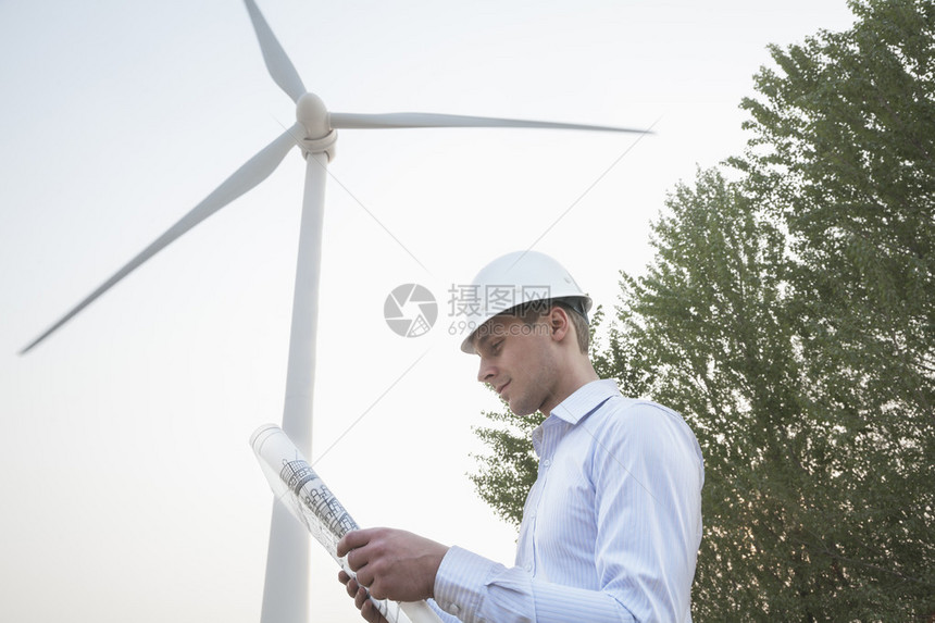 年轻男工程师身穿硬马帽看着风力涡图片