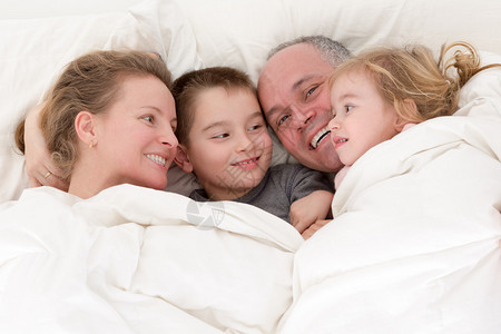 快乐的年轻家庭与一个漂亮的小女孩和她的兄弟在床上拥抱在一起图片