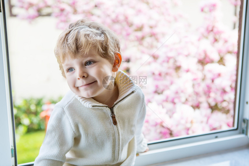 长着金发的可爱男孩坐着看窗外在室内图片