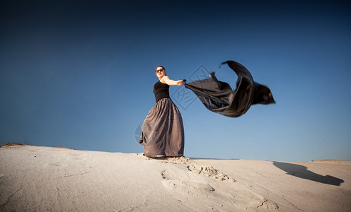 穿着黑布走在沙丘上的女人的照片图片