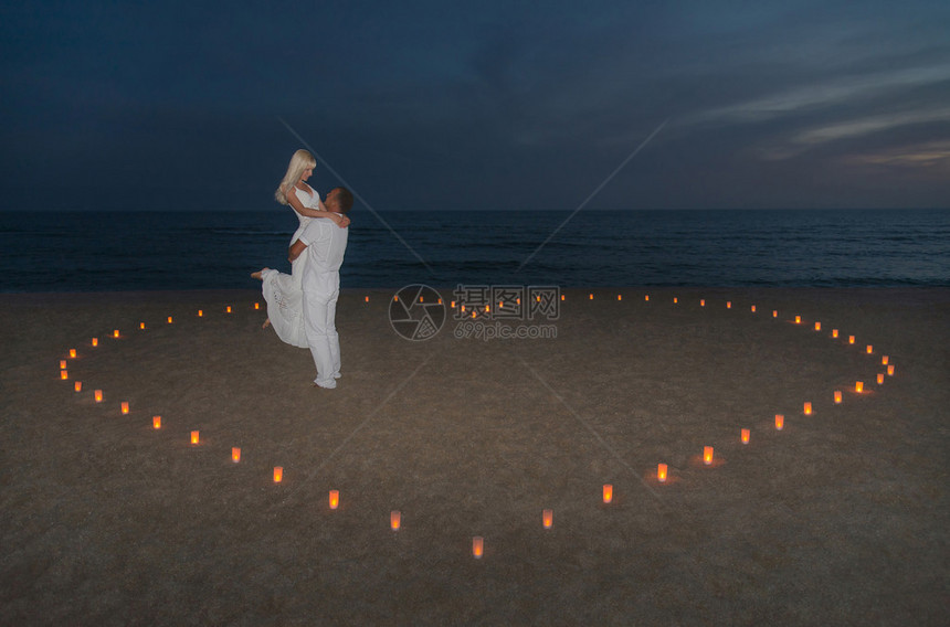 面对日落和圣瓦伦提斯节浪漫概念在海边滩的蜡烛心图片