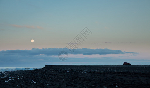 在日落时满月的Jokulsarlon海滩上长镜头长的旅游汽图片