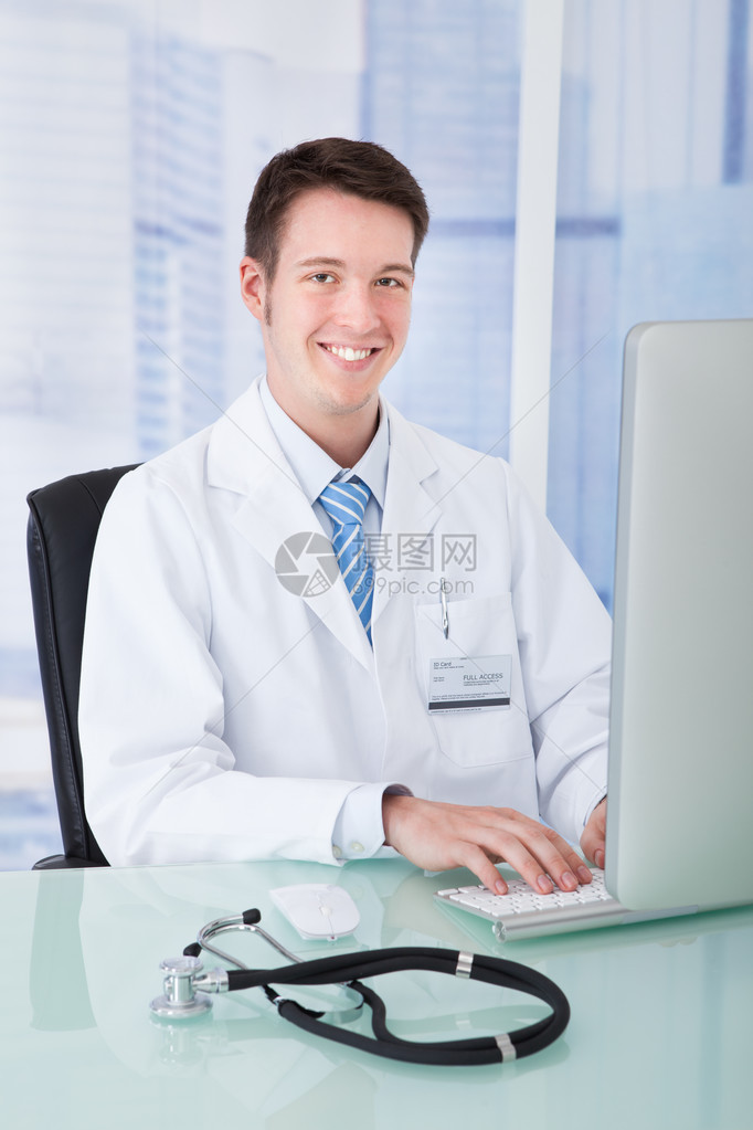 在诊所服务台使用计算机的年轻男医生充图片