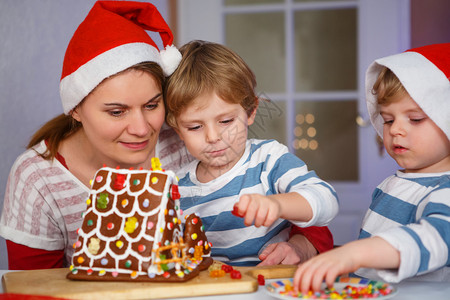 妈和两个小儿子在圣诞节准备一个姜饼干屋做圣图片