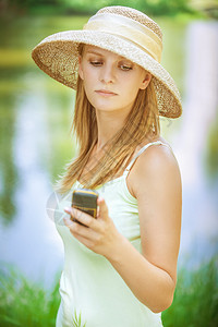 穿着草帽在湖边的年轻美女在城市公园里通过图片