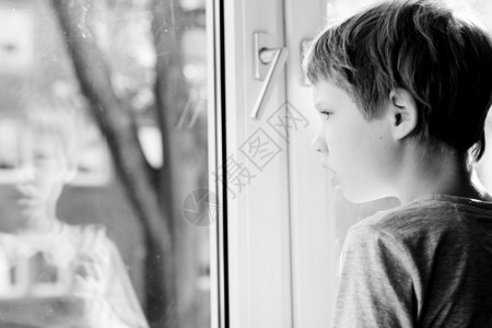 可爱的6岁男孩看着窗图片