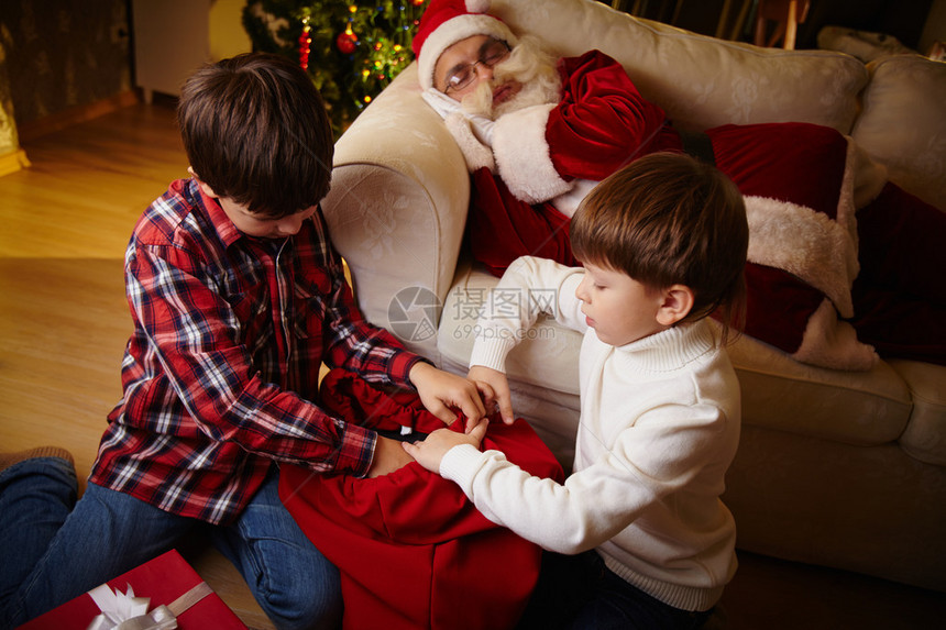 两个男孩选择了红袋的礼物圣诞老人睡在图片