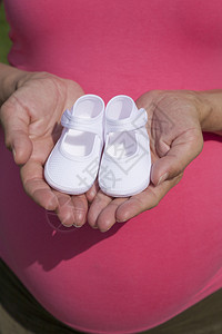 手拿婴儿短靴的粉色孕妇图片