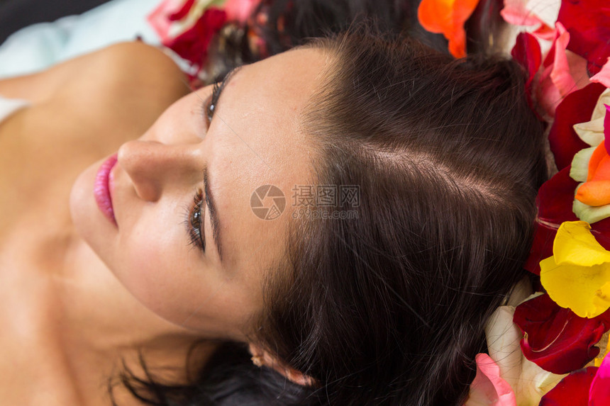 美容水疗面部在spa沙龙的美丽黑发女孩躺在美容院的玫瑰花瓣上美容图片
