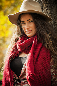 穿着帽子大衣和红围巾的长卷发微笑的年轻女子在公园图片