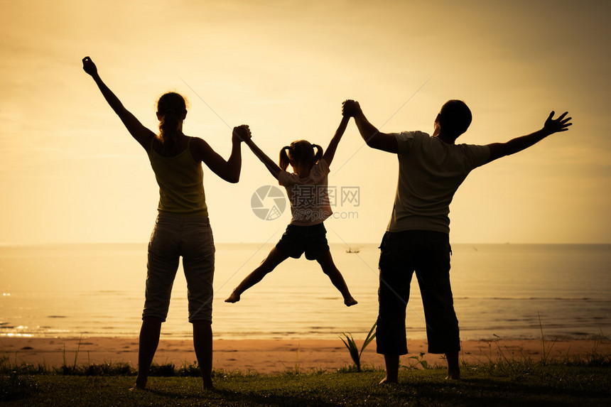 在日出时间站在海滩上的幸福家庭图片