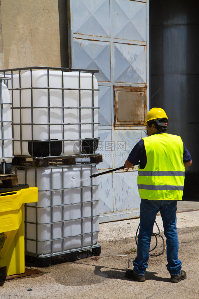身戴硬帽和安全背心的男工人在工业环境中用塑料容器在铁窗后图片