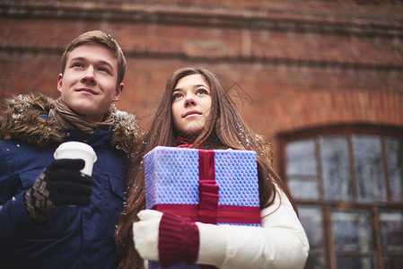 穿冬装快乐的年轻夫妇带礼品箱和咖啡塑料图片