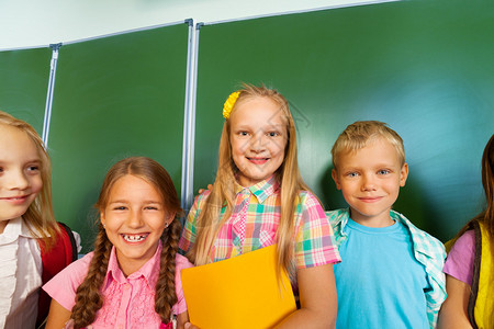 微笑的儿童与学校黑板附近的教科书站在一起图片