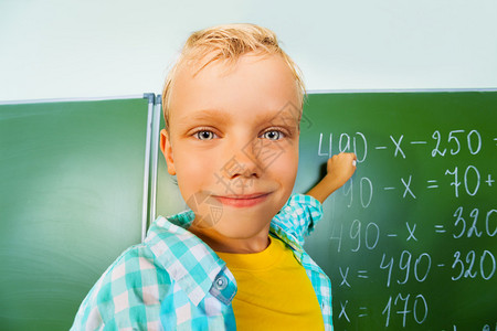 带着粉笔的男孩站在黑板旁边在数学课上图片