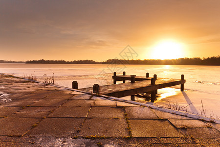 寒冷清晨日升在冰雪的冰冻冬湖上的喷图片