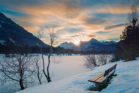 孤独公园的长椅上在时在阿尔卑斯山与在冬天结冰的湖面图片