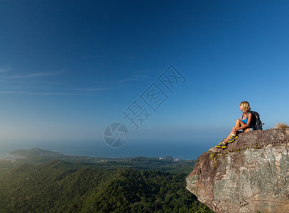 在阳光明媚的日子坐在山顶的年轻女图片