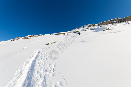 一群旅游滑雪者在陡峭的雪坡上徒步上山图片