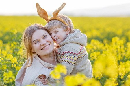 蹒跚学步的小孩和他的母亲在复活节兔子耳朵里玩得开心图片