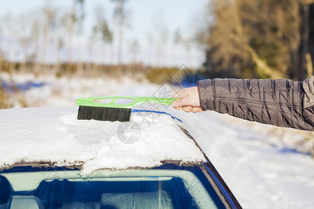 男人用刷子把车从雪地里打扫干净图片