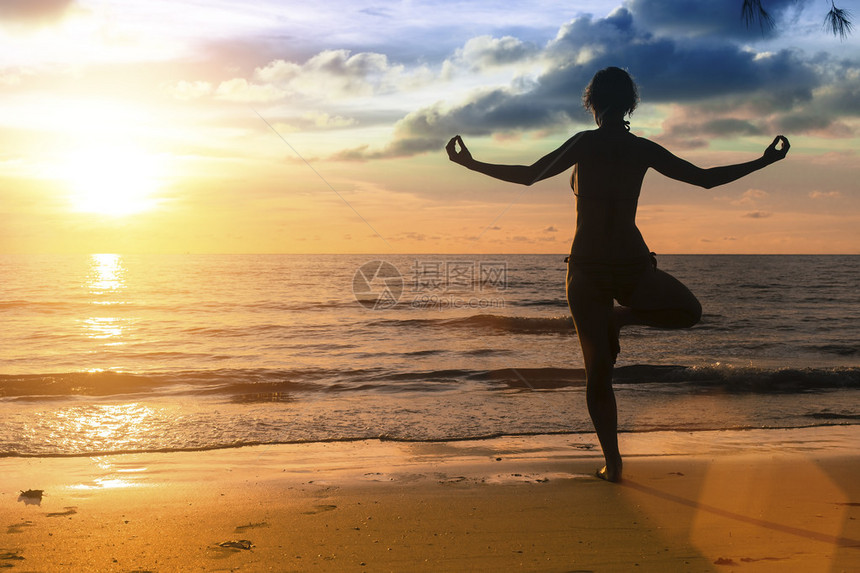 在海边令人惊叹的日落期间练习瑜伽的女人的剪影图片