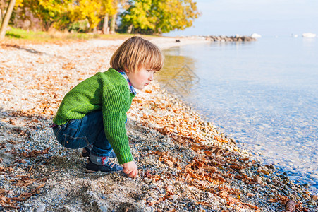 可爱的小孩男在湖边玩耍在温暖阳光明媚的天气中穿着绿色图片