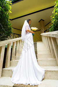 穿着婚纱和长列火车的美丽新娘站在热带岛屿上酒店的楼梯上图片