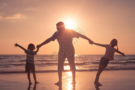 父亲和孩子们在日落的时候在海滩上玩耍友好家庭的概图片