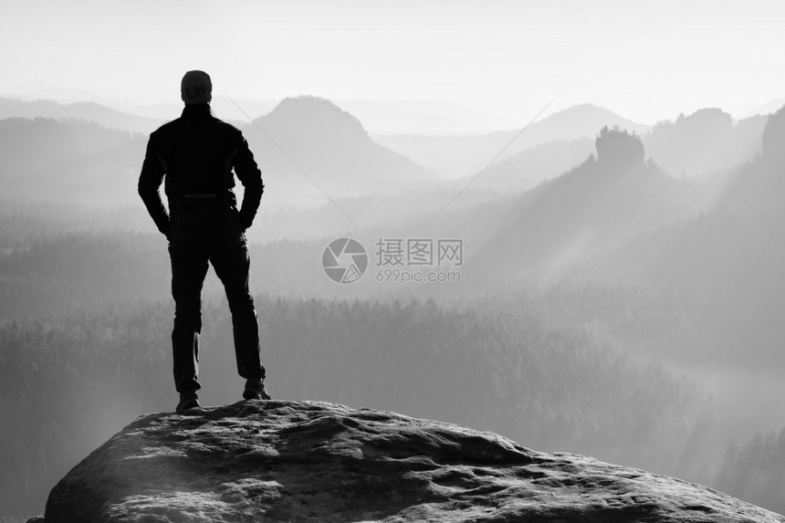 希克正站在岩石帝国公园的沙石岩峰顶上看着明晨微雾薄的山谷走向太阳美丽的瞬间图片