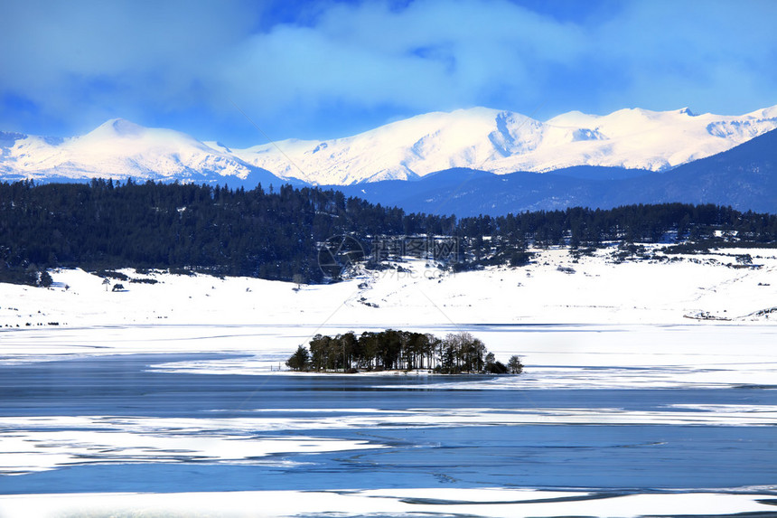 保加利亚高山的冰冻冬湖前景中的小岛和背景中覆图片
