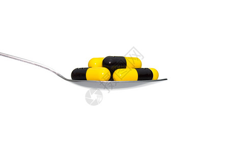 黑色黄药物或药丸或维生素在白色背景上孤立的金属勺子关于医疗保健或医疗图片