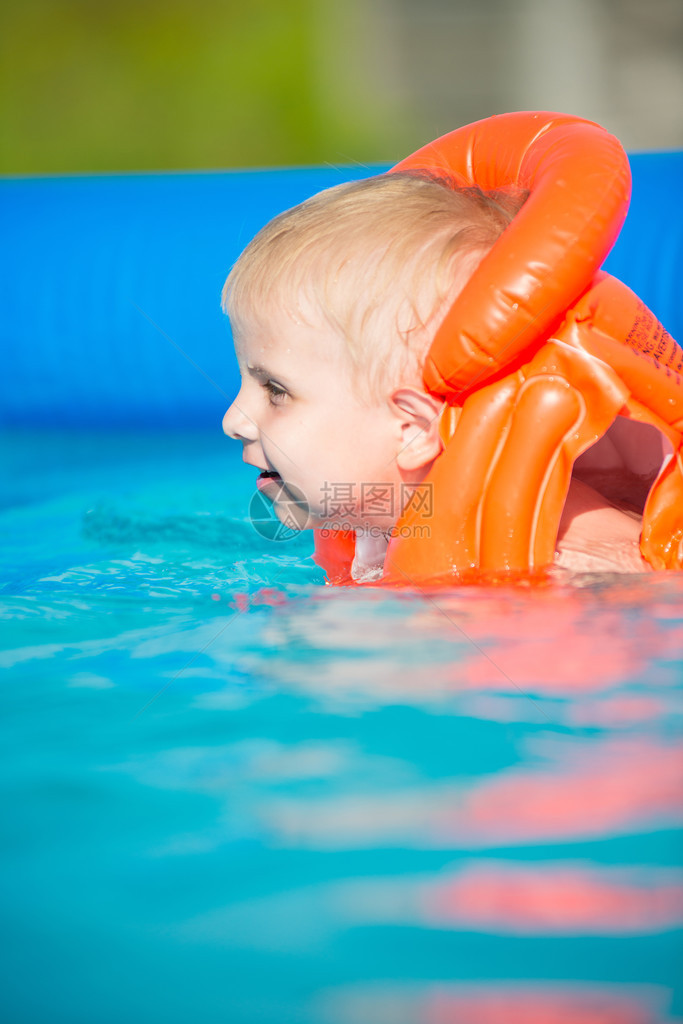 游泳池里漂亮的小男孩穿着橙色救生衣在户外图片