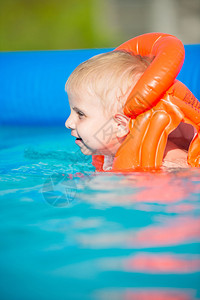 游泳池里漂亮的小男孩穿着橙色救生衣在户外图片