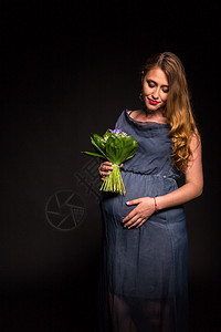 美丽的孕妇与黑色背景上的花朵图片
