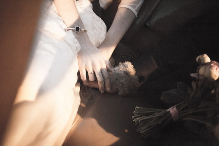 新郎穿着深色西装和白色衬衫在婚礼中与穿着白色长婚纱的新娘手牵的彩色图片