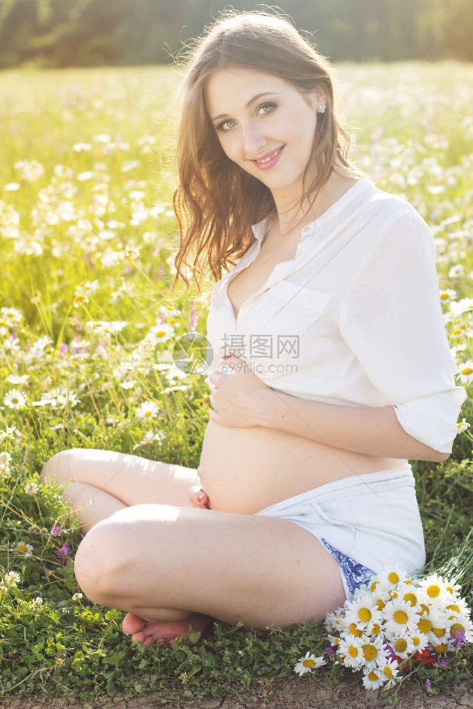 快乐的孕妇坐在甘菊花草地上日落时间图片