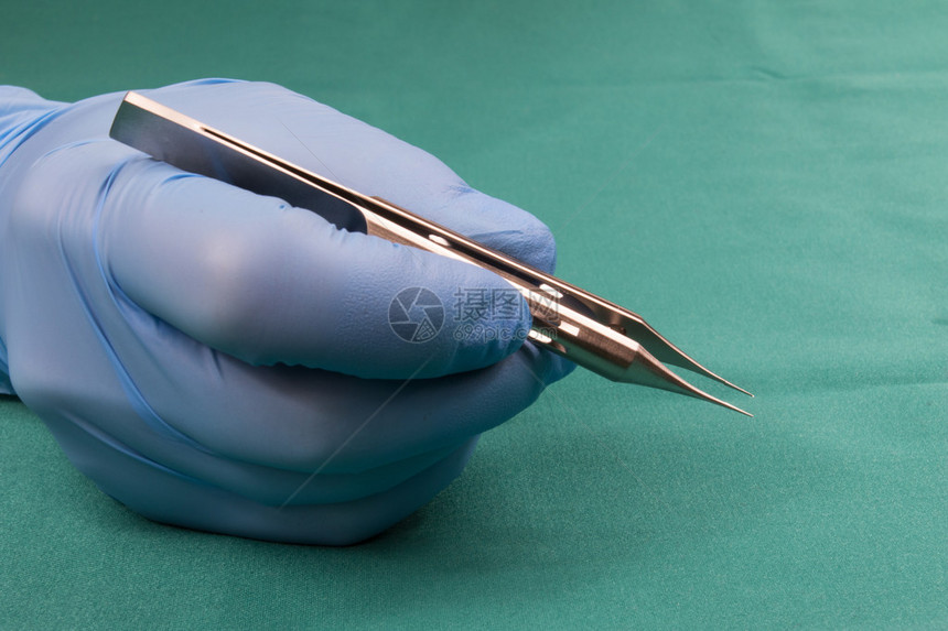外科医生手持微型手术工具外科医生手戴蓝色手套外科医生直接用平台握住帽子背景是图片