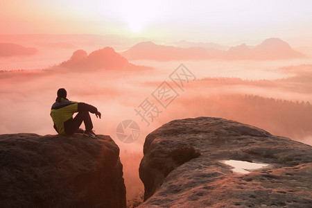 雄徒步者坐在山顶的岩石峰上的后视线图片