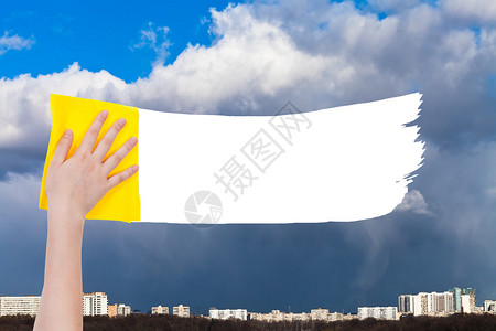 手从图像上用黄色抹布删除城市上空的雨云图片