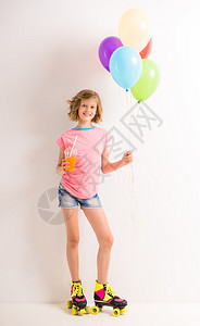 穿着溜冰鞋的漂亮女孩拿着彩色气球和杯子汁图片