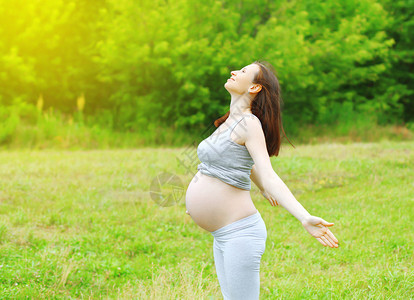 快乐的孕妇在草地上享受阳图片