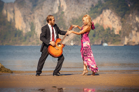 穿着高脚跟鞋的金发舞女金发女孩背影和胡子吉他手在海滩对图片