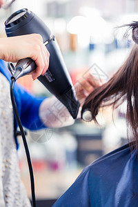 女理发师在店里用吹风机吹干女头发图片