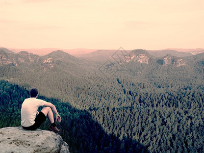 孤独的时刻穿衬衫的旅游者坐在岩石顶峰上图片